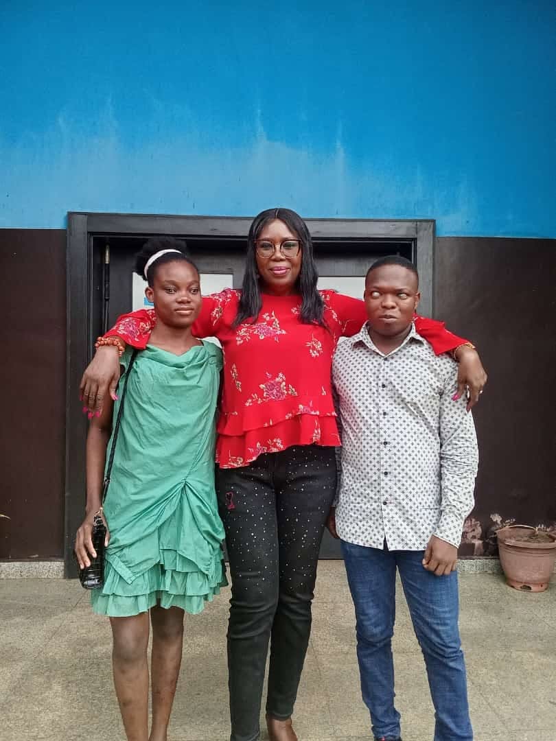 Three members of the Ifite community, one of whom is visually impaired, standing together outside.